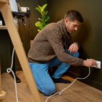 Homeowner ensuring electrical safety at home such as outlets and power cords in a living room.